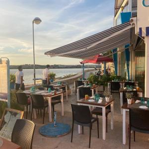 ein Restaurant mit Tischen und Stühlen und Blick aufs Wasser in der Unterkunft Prainhaactivitiesbeachhouse in Alvor