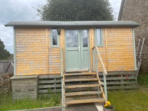 a tiny house with a green door and a ladder at Jackdaws Shepherds Hut in Epwell