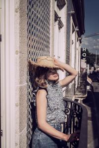 a woman sitting on a balcony wearing a straw hat at Original Douro Hotel in Peso da Régua