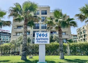a sign in front of a building with palm trees at Teos Apartments Primorsko in Primorsko