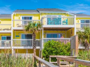 a yellow house with white balconies and palm trees at Ocean Dunes 1402 in Kure Beach