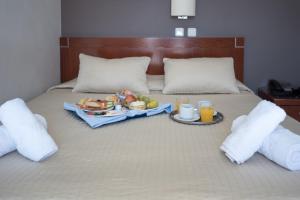 a tray of food on a bed with two drinks at Epidavros Hotel in Athens