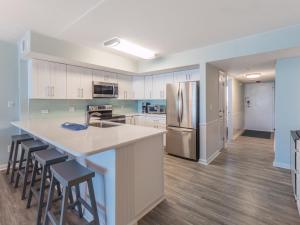 una cocina con armarios blancos y una gran isla con taburetes. en Pelican Watch #806, en Carolina Beach