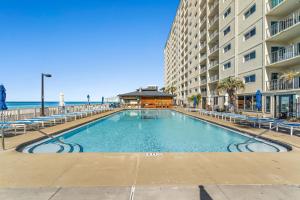 a swimming pool in front of a building and the ocean at 4 Loungers 2 Umbrellas Inlc Peak Season Beachfront in Panama City Beach