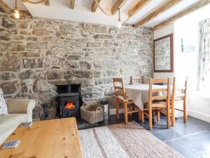 una sala da pranzo con pareti in pietra, un tavolo e un camino di Ivy Cottage a Harlech