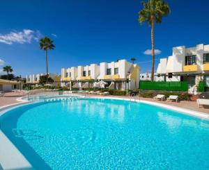 a large blue swimming pool with palm trees and buildings at Bungalow Capri Maspalomas in San Bartolomé