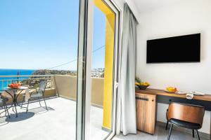 a room with a balcony with a desk and a television at Apolis Beachscape Hotel in Amoopi