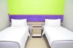 two twin beds in a room with green and purple at Alodia Powered by Archipelago in Tanjungkarang +2 photos