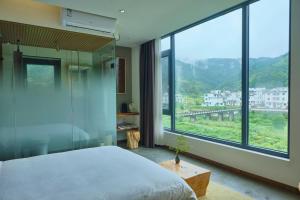 um quarto com uma cama e uma janela grande em Nature Cure Village Lodge-婺源自在舍 em Wuyuan