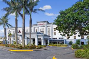 a white building with palm trees in front of it at Hampton By Hilton San Jose Airport Costa Rica in Alajuela City