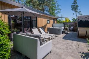a patio with an umbrella and chairs and a grill at Wellnesslodge Grutto in Dalerveen