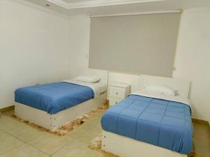 Alojamiento San Cayetano في لوخا: سريرين في غرفة بيضاء مع ملاءات زرقاء