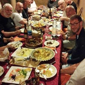 a group of people sitting around a long table with food at Maison Merzouga Guest House in Merzouga