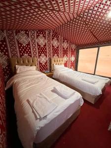 two beds in a room with a red wall at Obeid's Bedouin Life Camp in Wadi Rum