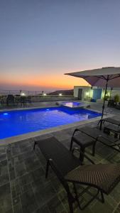 a swimming pool with two benches and an umbrella at Ayla Chalets in Amman