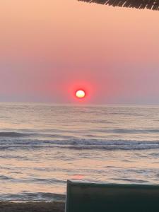 a sunset over the ocean with a chair on the beach at Apartment Gerti - Sea view in Shëngjin +3 photos