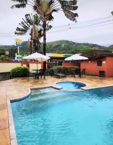 a swimming pool in a resort with tables and umbrellas at Flat em Juquehy - Condomínio com portaria e com piscina próximo praia in São Sebastião