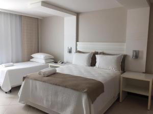 a white bedroom with two beds and a table at Violeta Meaípe Hotel in Guarapari