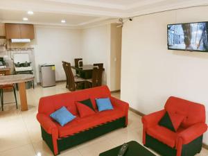 a living room with two red chairs and a kitchen at Departamento El Rosal 2 in Cuenca