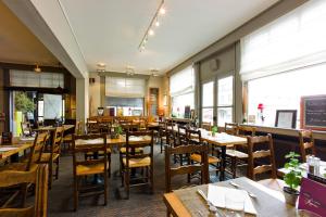 a restaurant with wooden tables and chairs and windows at The Originals Boutique, Hôtel Auberge du Forgeron, Lille Sud in Seclin