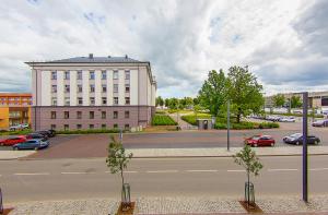 Una calle con un gran edificio blanco y coches en la carretera. en Butas Šiaulių mieste, en Šiauliai