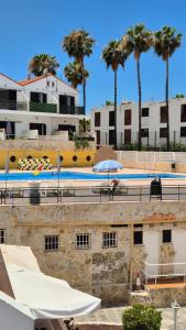 a swimming pool with umbrellas and buildings and palm trees at Appartamento Altamar Las Americas in Playa de las Americas