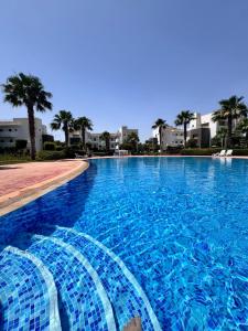 a large blue swimming pool with palm trees and buildings at Résidence perla, piscine, bord de plage in Saïdia