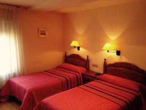 two beds in a hotel room with red sheets at Hostal Nicolás in Medinaceli