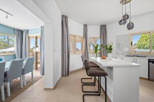 a kitchen with white counters and chairs and windows at Harmonia Luxury Villa by Nomads in Peyia