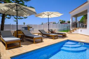 a pool with chairs and umbrellas next to a house at Harmonia Luxury Villa by Nomads in Peyia