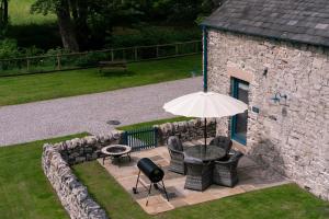 un patio avec une table, des chaises et un parasol dans l'établissement Dipper Cottage Upperdale Peak District, à Buxton