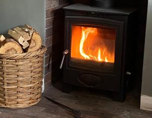 una stufa a legna con un cesto di legna di The Old Post Office, Cosy Cottage in Northumberland, Near Coast, Dog Friendly a Chatton