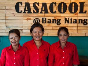 Tre donne in camicie rosse davanti a un cartello di Casacool Hotel a Khao Lak