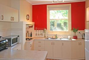 cocina con paredes rojas, lavabo y ventana en Oats Cottage, en Hahndorf