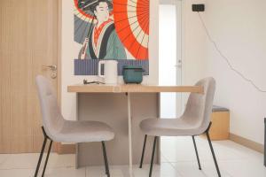 a table with two chairs and a painting on the wall at Well Furnished and Restful 2BR Tokyo Riverside PIK 2 Apartment By Travelio in Rawalembang