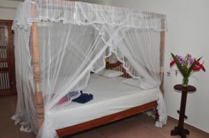 a canopy bed with white curtains and a vase of flowers at SurfCity Guesthouse in Unawatuna