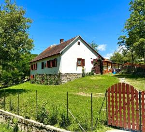 a white house on a hill with a fence at Pensiunea Casa Țărănească in Satu Bătrîn