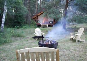 a grill with two chairs and a tent in the woods at Glempings Eglenieki in Almale