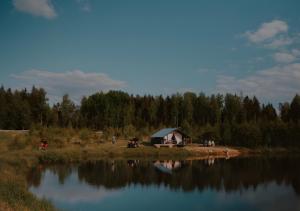 Una pequeña cabaña al lado de un lago con gente alrededor. en Glempings Dīķīši, en Stākas
