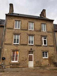 un antiguo edificio de ladrillo con puertas y ventanas blancas en Grand Studio Ceo Bauer, en plein centre de Sainte-Mère-Eglise pour 2 pers, en Sainte-Mère-Église
