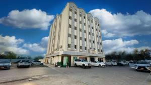 a large white building with cars parked in a parking lot at Star Dahlia Hotel in Muscat