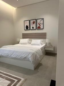 a bedroom with a white bed with three pictures on the wall at Luxury Modern Apartment with Gym and Lounge in Riyadh