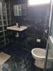 e bagno piastrellato nero con servizi igienici e lavandino. di Elite Serviços Lda a Chibungo