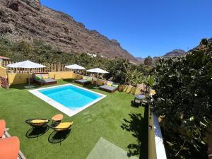 a backyard with a swimming pool with chairs and umbrellas at SUNNY CARMELITO DELUXE in Mogán