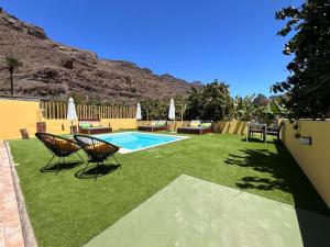 a backyard with a swimming pool and chairs and a lawn at SUNNY CARMELITO DELUXE in Mogán