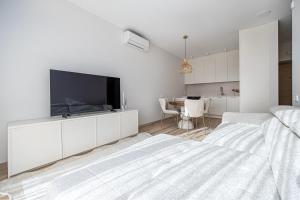 a white bedroom with a flat screen tv on a white cabinet at Vanagupės Perlas in Palanga