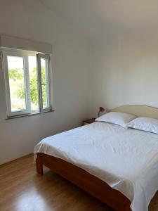 a white bedroom with a bed and a window at Apartments Anka Brala in Posedarje