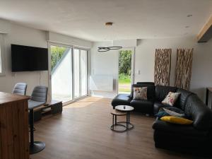 ein Wohnzimmer mit einem schwarzen Ledersofa und einem TV in der Unterkunft Jolie maison proche plages et golf in Bénodet