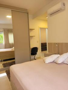 ein Schlafzimmer mit einem weißen Bett und einem Spiegel in der Unterkunft Apartamento Residencial Mar Azul - praia de Palmas - Governador Celso Ramos-SC in Governador Celso Ramos