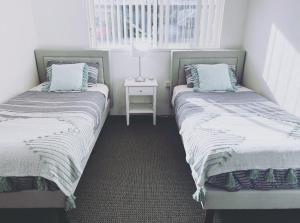 two twin beds in a room with a night stand at Nautilus Hamptons Style Beach Apartment Merimbula in Merimbula